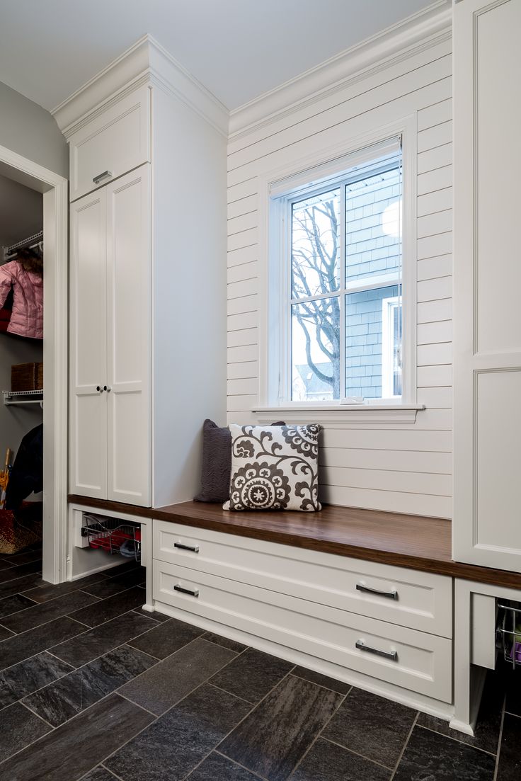 a walk in closet with white cabinets and black tile flooring, along with a bench