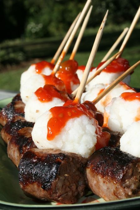 several skewered steaks with sauce and white rice on a green platter