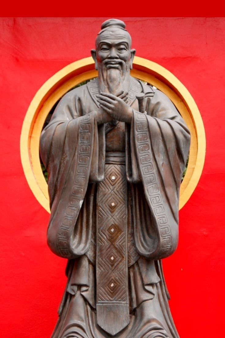 a statue of a man with his hands clasped in front of a red wall and gold circle