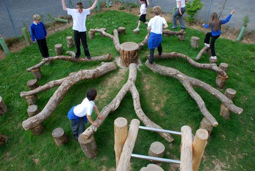 children playing with wooden logs in an outdoor play area that looks like a tree stump