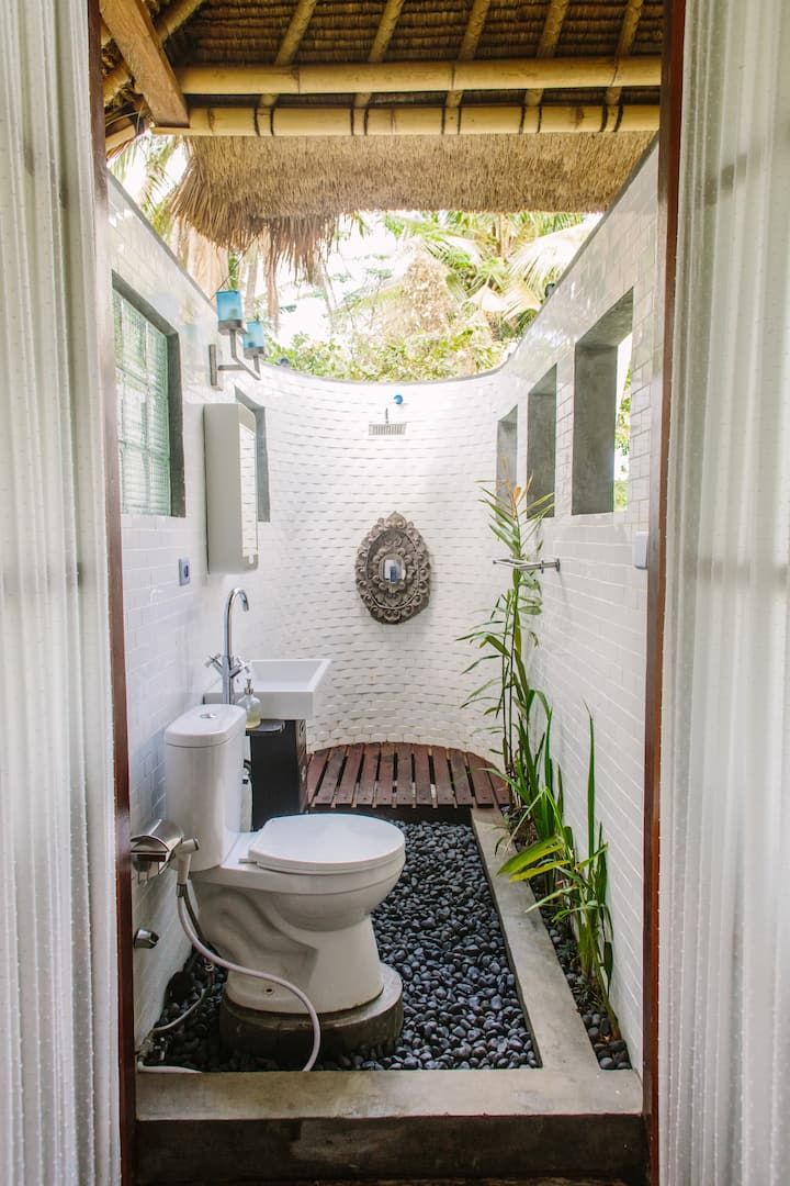 a white toilet sitting inside of a bathroom next to a bamboo roof over a sink