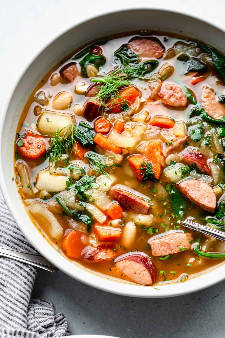 a bowl of kielbasa soup with carrots, potatoes and spinach in it