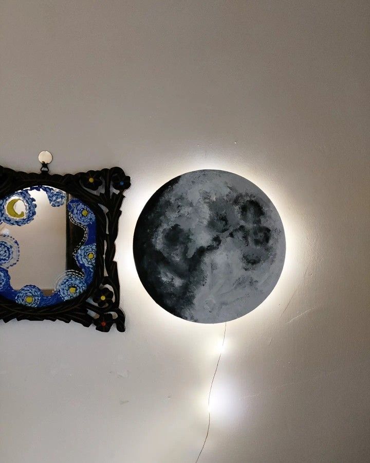 a clock with the moon behind it on a wall next to a light up frame