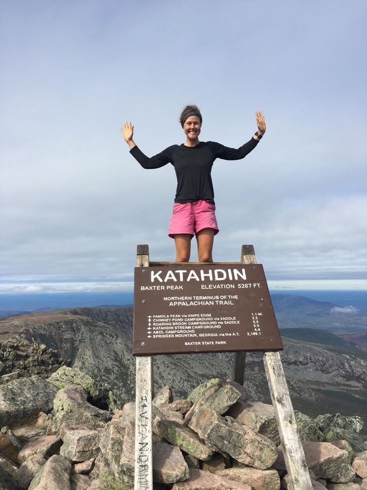 a woman standing on top of a sign at the top of a mountain with her hands in the air