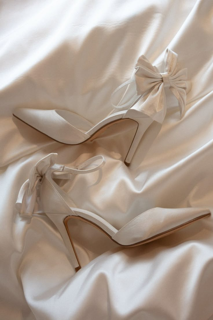 two pairs of white high heeled shoes laying on top of a white satin sheet