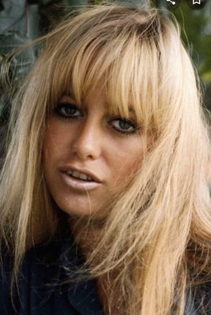 a woman with long blonde hair is posing for a photo in front of some trees