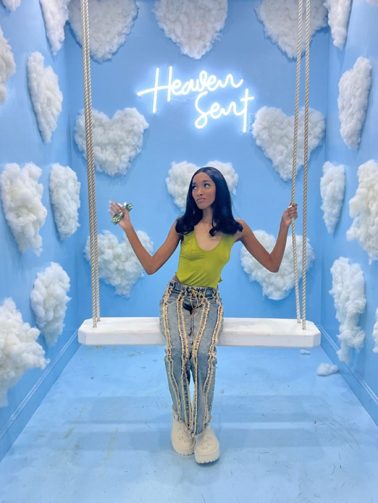 a woman standing on a swing in front of a blue wall with clouds and hearts