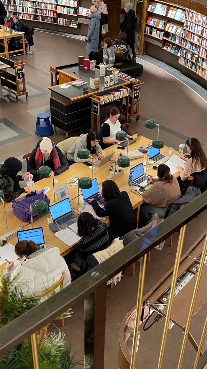 people sitting at tables in a library with laptops