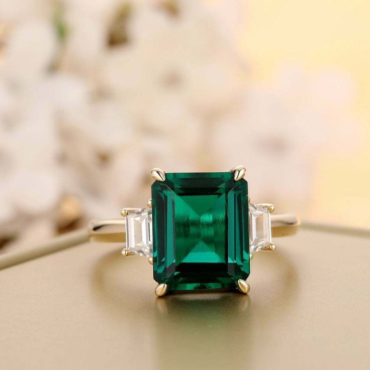 an emerald and diamond ring sitting on top of a table