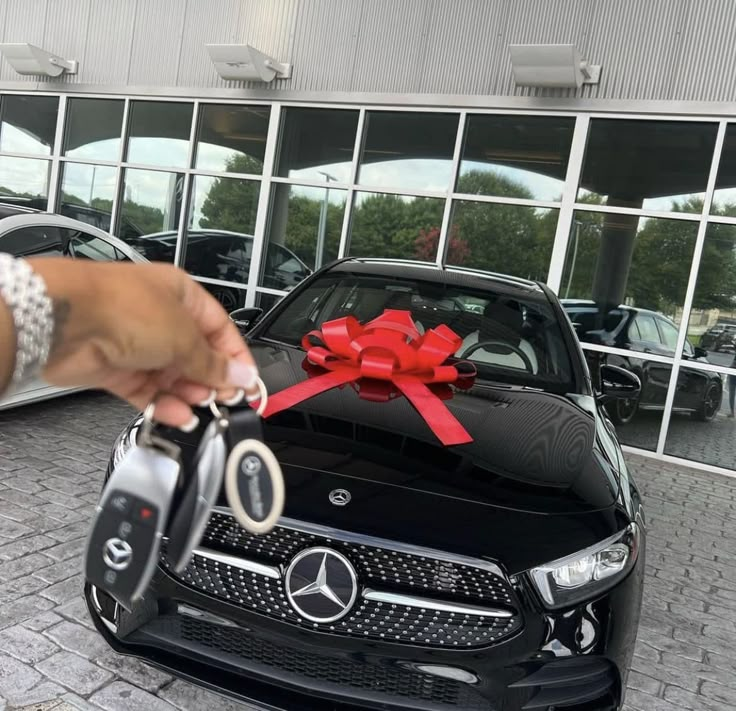 a person holding a car key in front of a mercedes dealership with a red bow on it