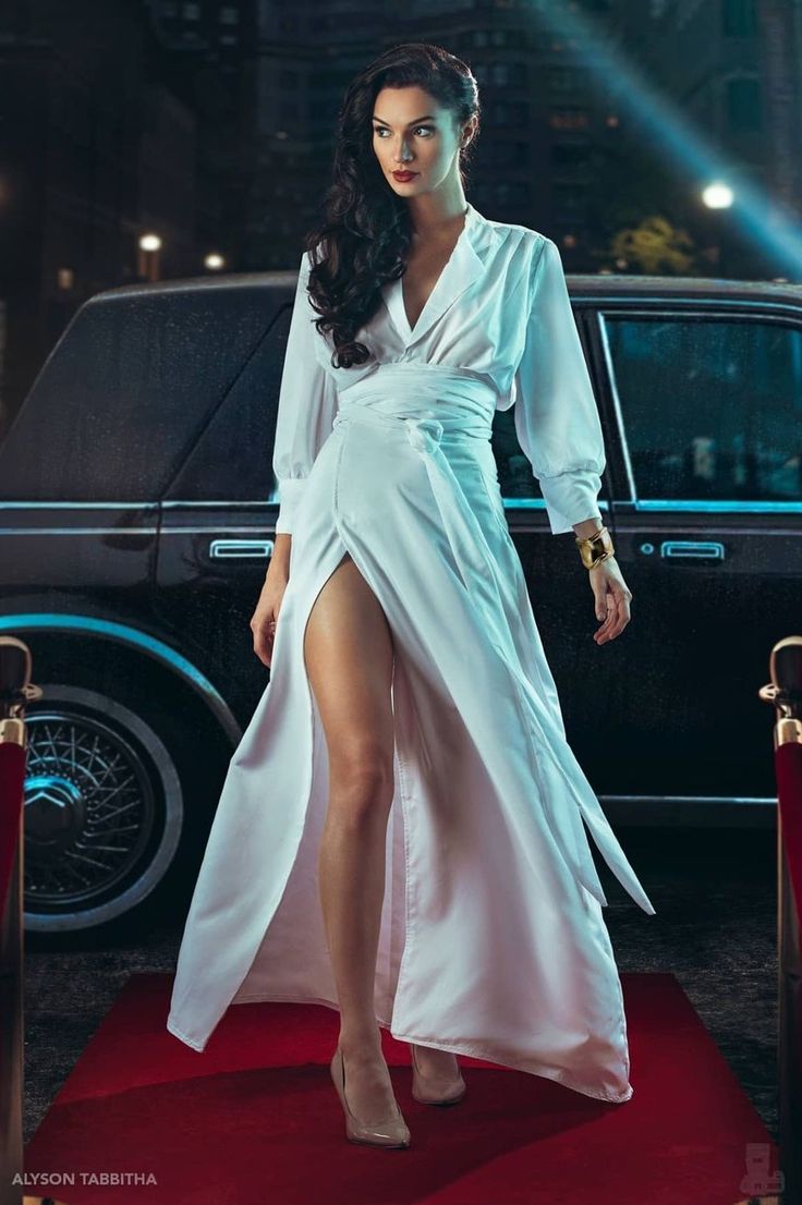 a woman in a white dress standing on a red carpet next to a black car