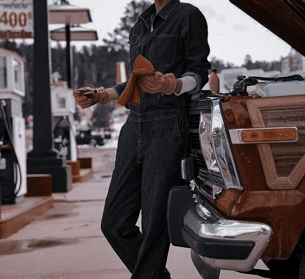 a man standing next to his car with gloves on and holding something in his hand