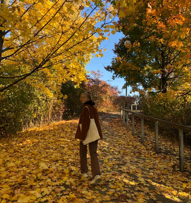 a woman standing in the middle of a leaf covered road