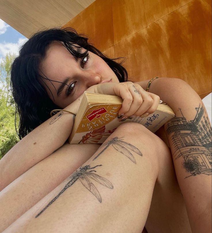 a woman with tattoos on her legs is laying down and holding a box of cheese