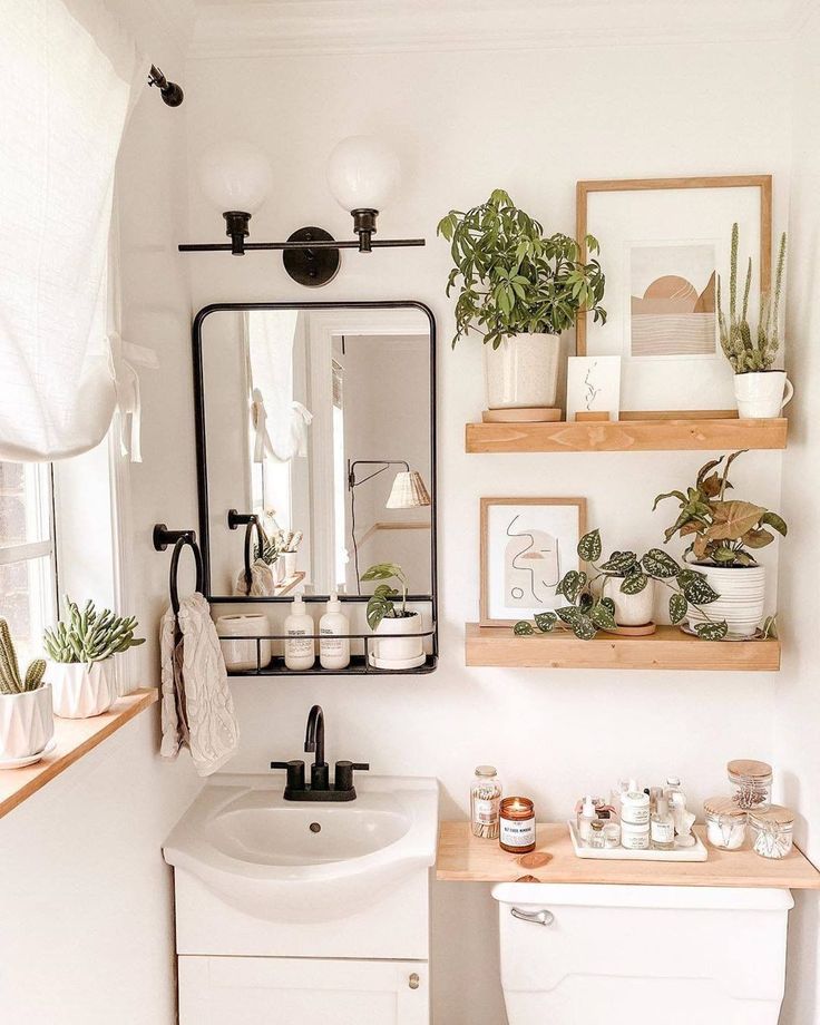 a white bathroom with plants and pictures on the wall above the toilet, along with a sink