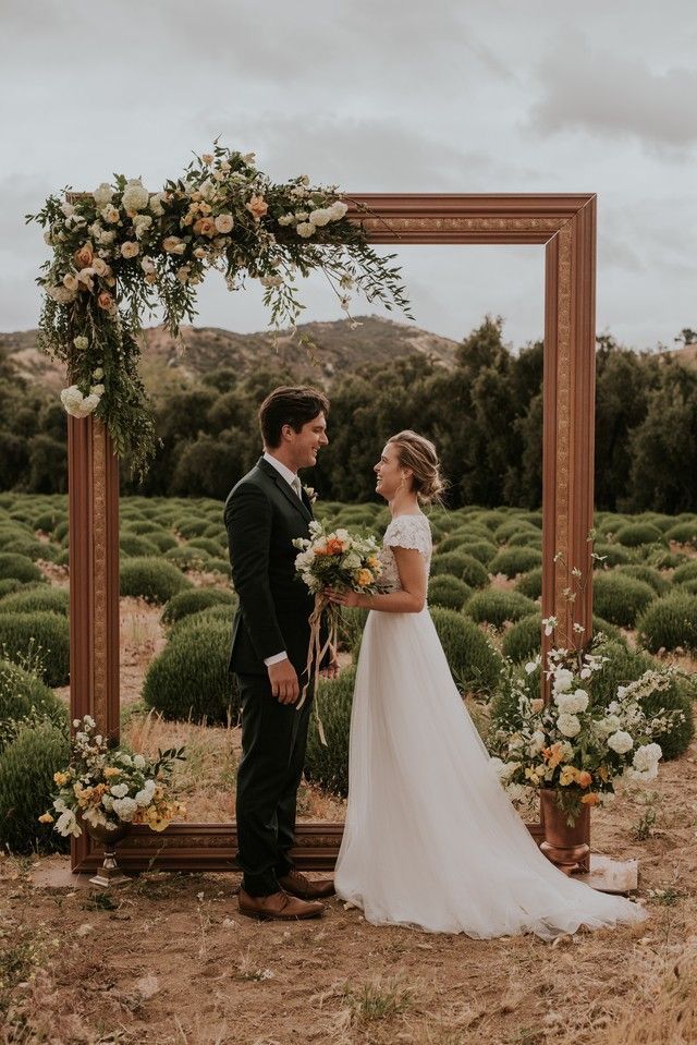 a bride and groom standing in front of an arch decorated with greenery for their wedding ceremony