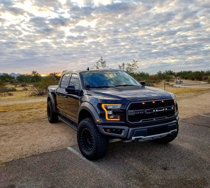 a large black truck parked on top of a parking lot next to a dirt field