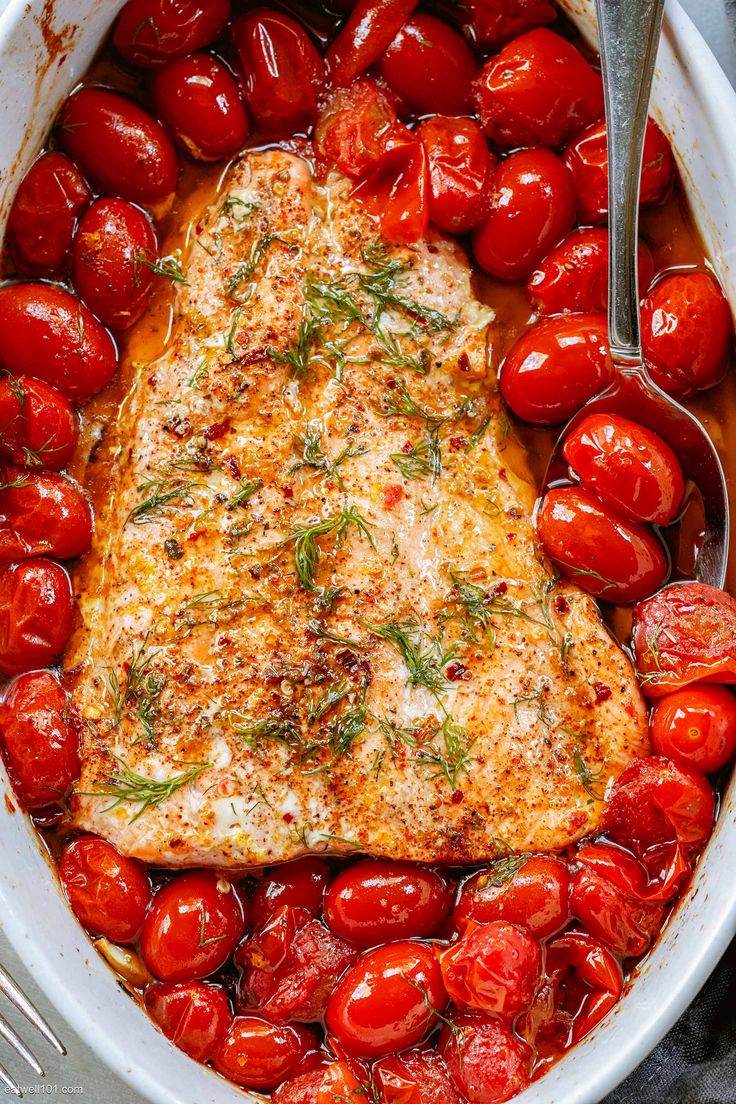 a white dish filled with tomatoes and topped with a piece of fish covered in herbs