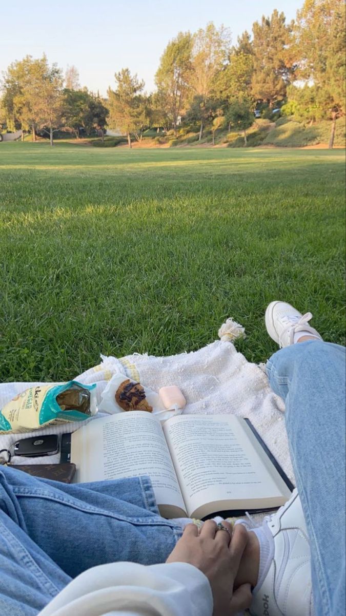 a person sitting in the grass with an open book and some books on their lap