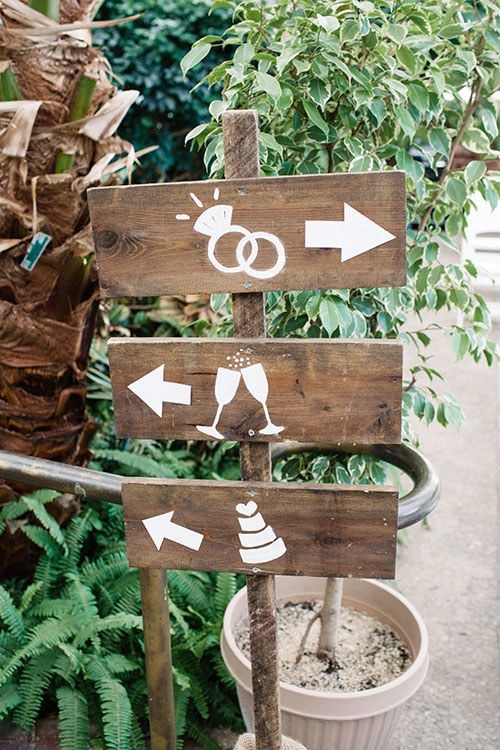 a wooden sign with arrows pointing in different directions and two wedding rings painted on it