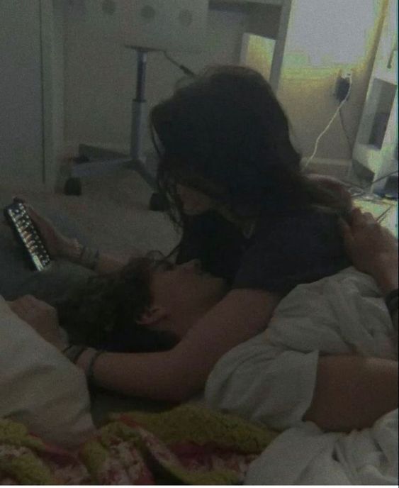 two people laying on a bed looking at an electronic device