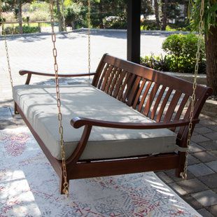 a wooden swing bed sitting on top of a white and pink rug next to a tree