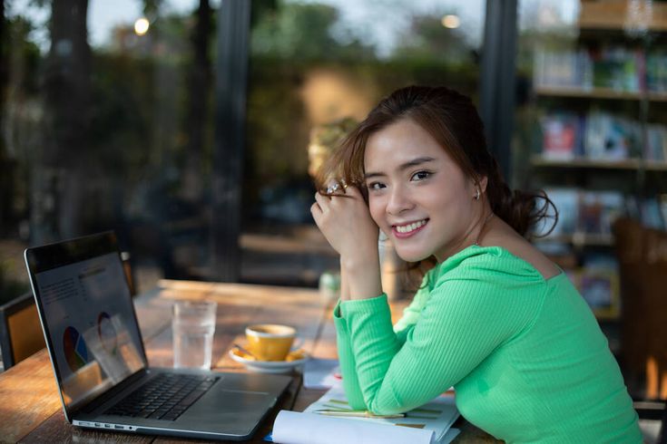 a woman sitting at a table in front of a laptop computer with her hand on her chin