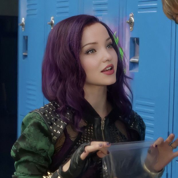 a woman with purple hair is holding a plastic container in front of lockers and talking to someone