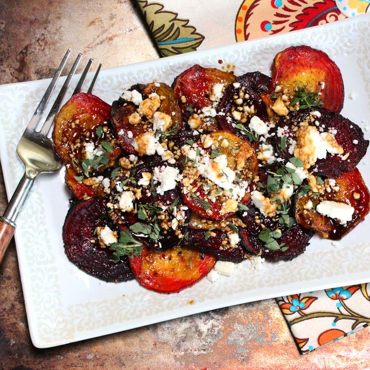 a white plate topped with fruit and feta cheese next to a knife and fork