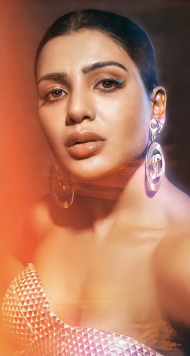 a woman with large earrings on her neck posing for a photo in front of an orange and yellow background