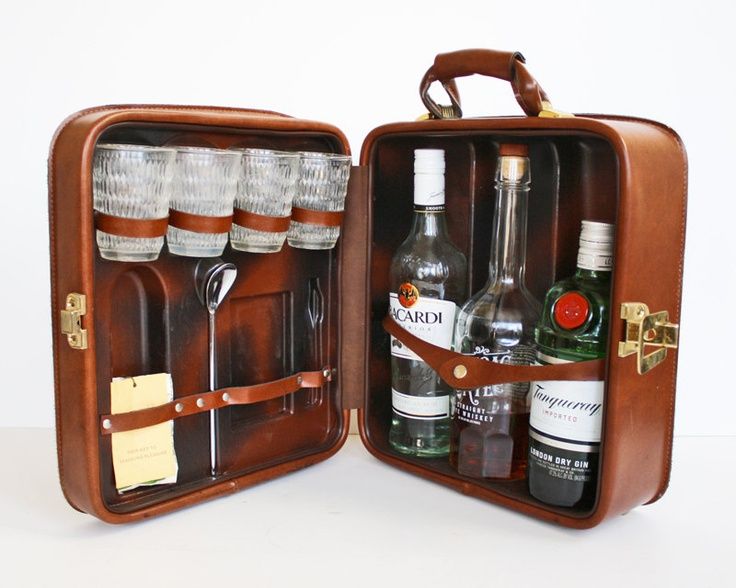 an open suitcase filled with liquor bottles and glasses on top of a white table next to a bottle opener