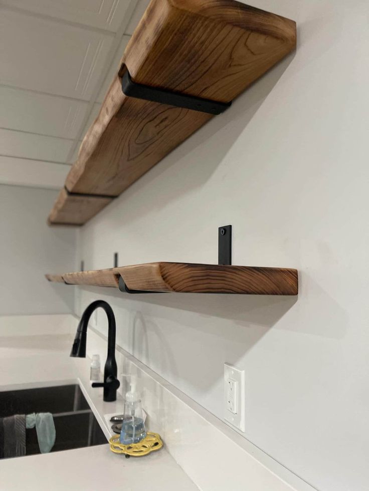 two wooden shelves on the wall above a sink in a room with white walls and black faucets