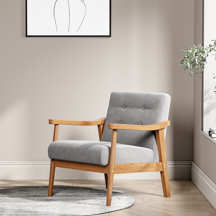 a gray chair sitting on top of a wooden floor next to a white vase filled with flowers