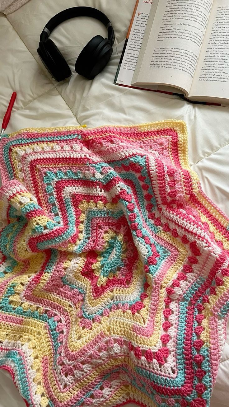 a crocheted blanket and headphones on top of a bed next to an open book