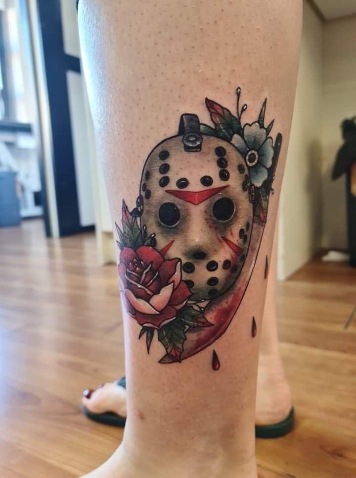 a tattoo on the leg of a person with a mask and roses around it,