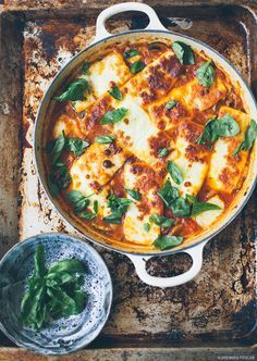 a pan filled with cheese and spinach on top of a wooden tray next to two bowls