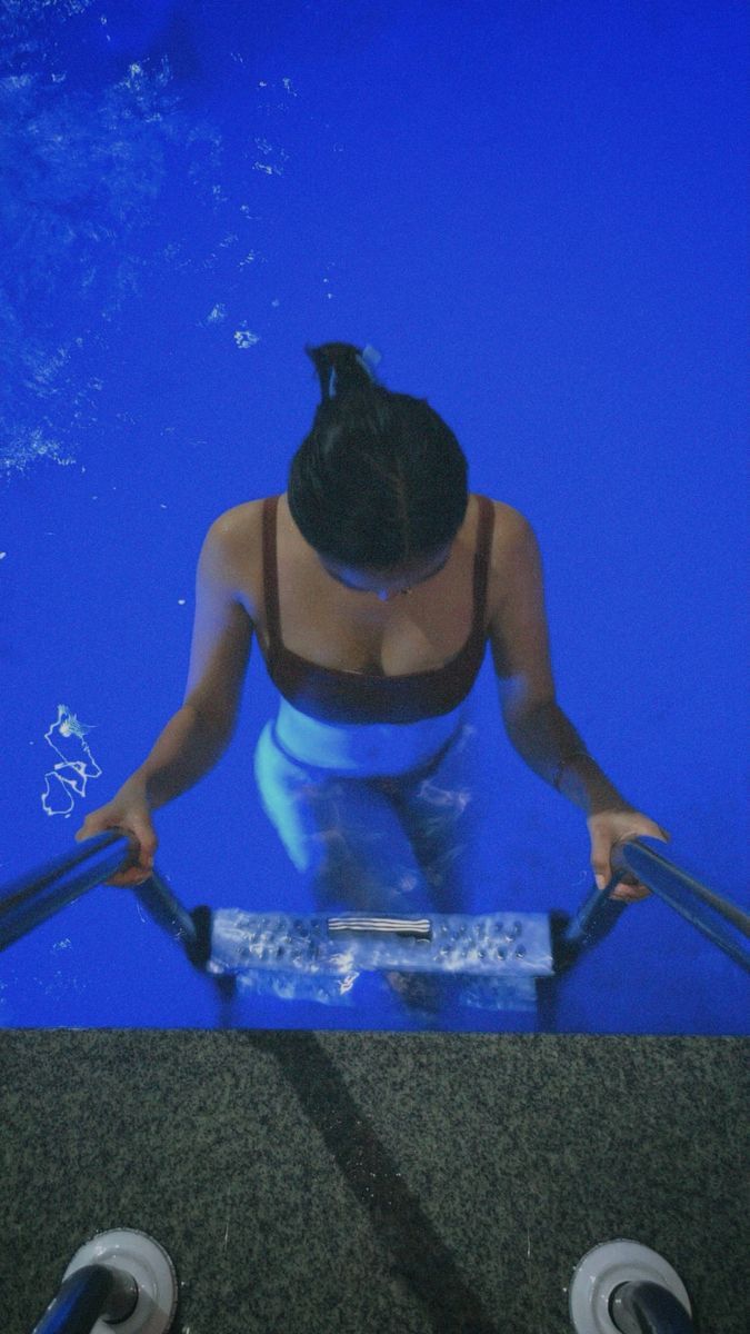 a woman standing in front of a swimming pool with her hands on the edge of an electronic device