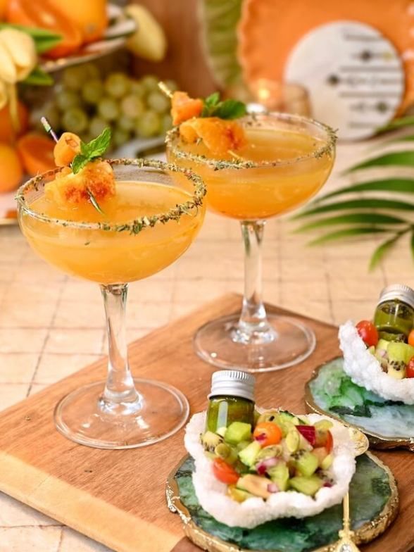 two glasses filled with drinks sitting on top of a cutting board