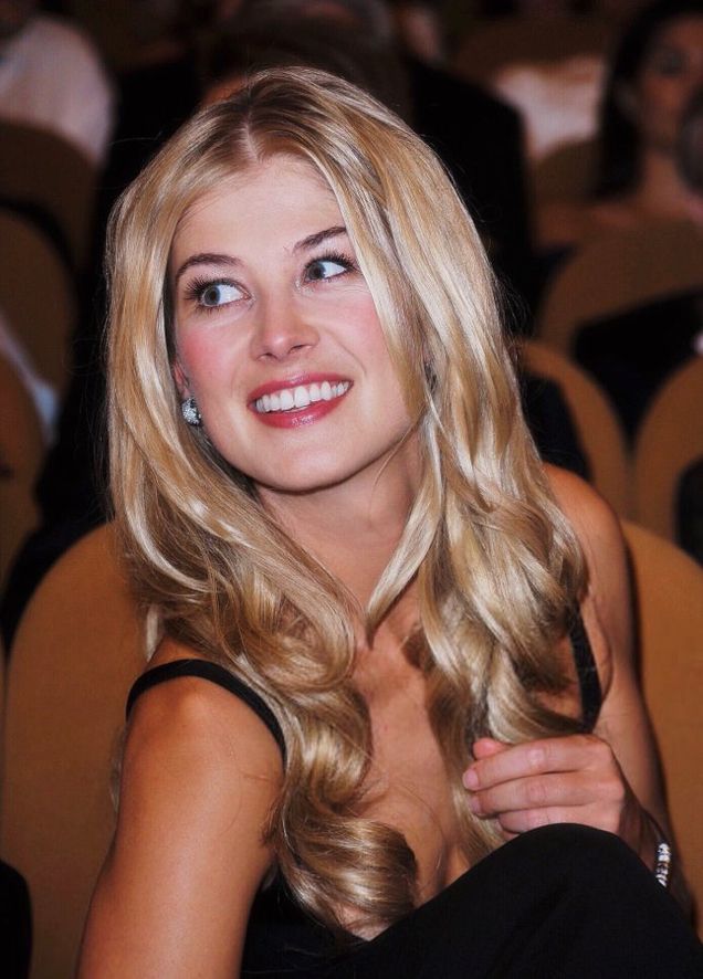 a woman with long blonde hair sitting in a chair and smiling at the camera while wearing a black dress