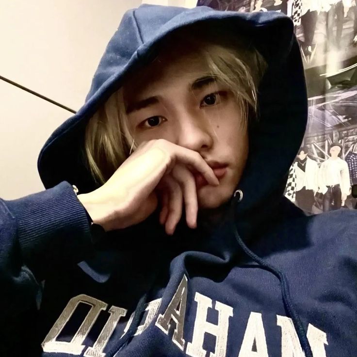 a young man wearing a blue hoodie and posing for the camera with his hand on his chin