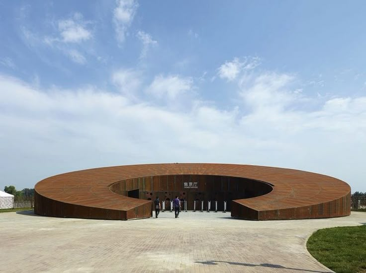 two people are standing in front of a circular structure on a concrete area with grass and blue sky