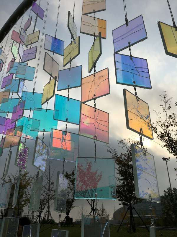 many different colored glass pieces hanging from the side of a metal structure with trees in the background