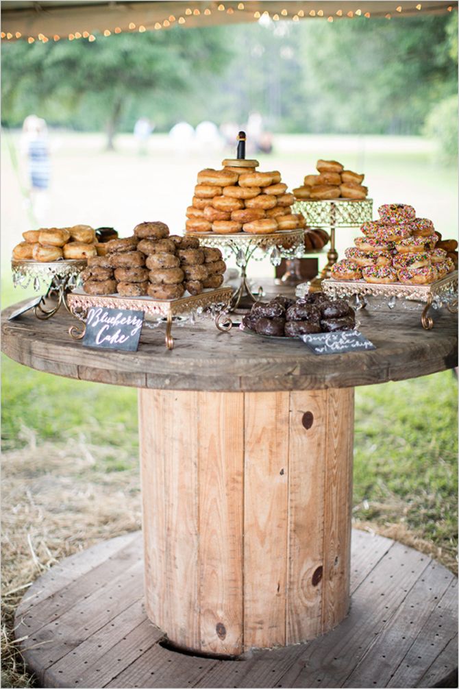 a table topped with lots of donuts and pastries on top of a wooden barrel