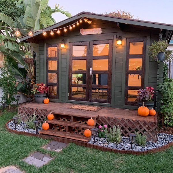 a small green shed with lights on the roof and some pumpkins in the yard