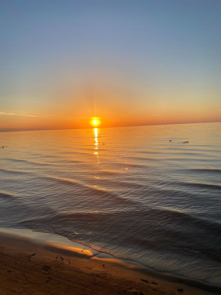 the sun is setting over the water at the beach