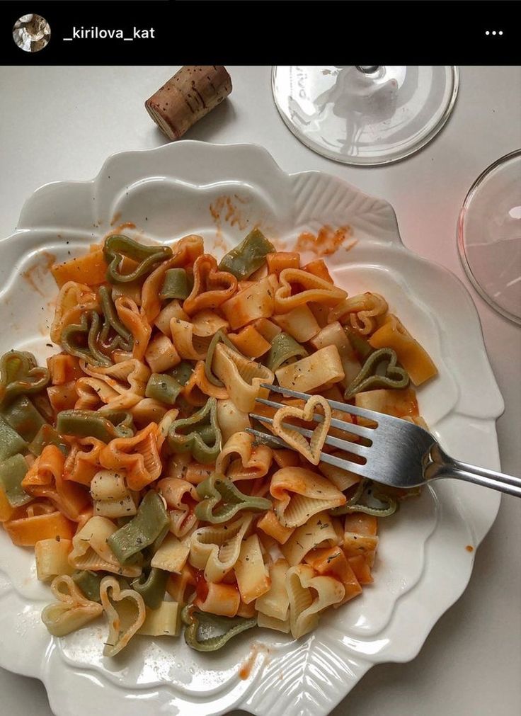 a white plate topped with pasta and veggies next to a glass of wine