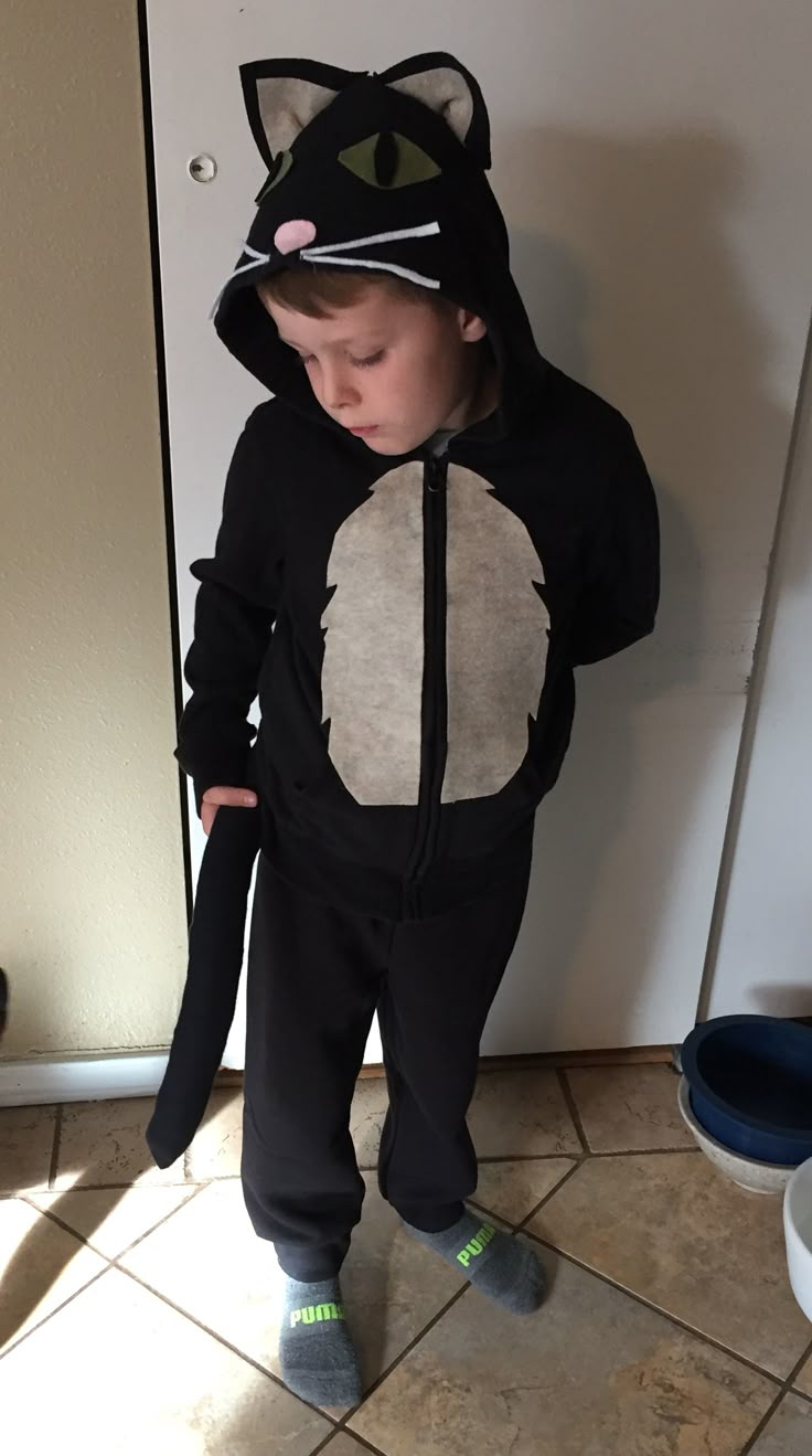 a little boy in a cat costume standing next to a door and looking at the camera