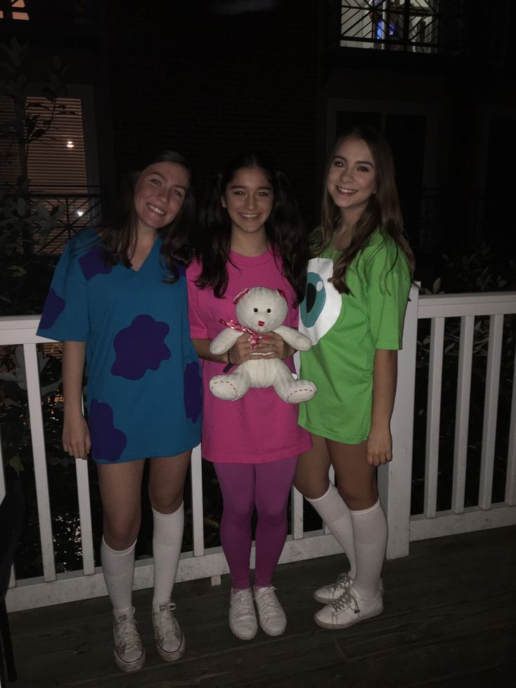 three girls are standing on a porch with one holding a teddy bear and the other wearing colorful clothing