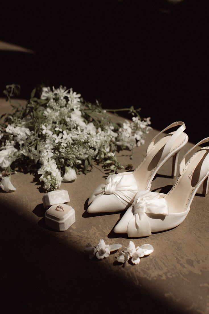 a pair of white shoes sitting on top of a table next to flowers and jewelry