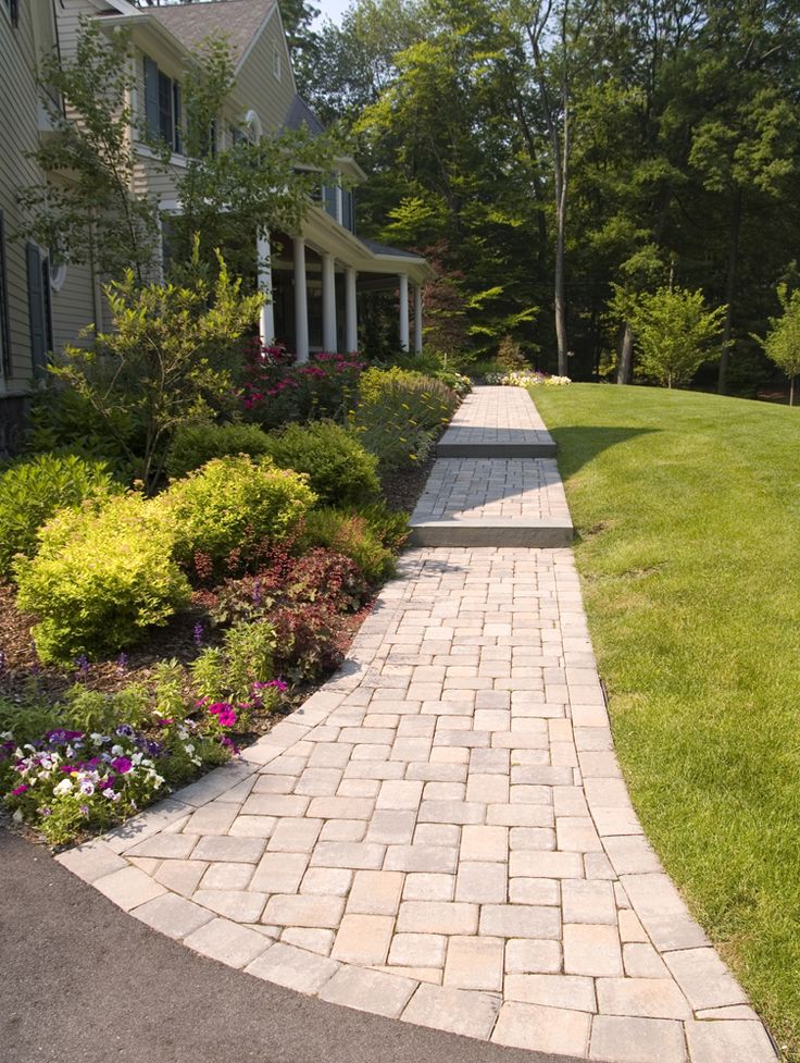 a brick walkway in front of a house surrounded by lush green grass and flowers on either side